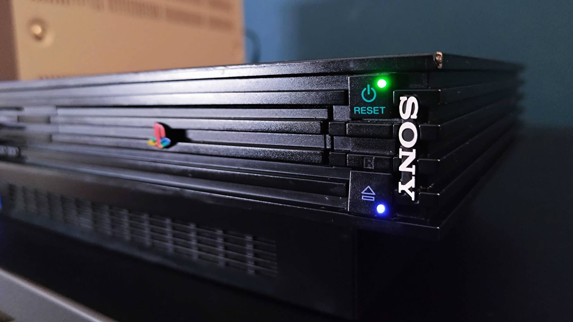 Close up of original PS2 switched on with green reset and blue eject button lights illuminated.